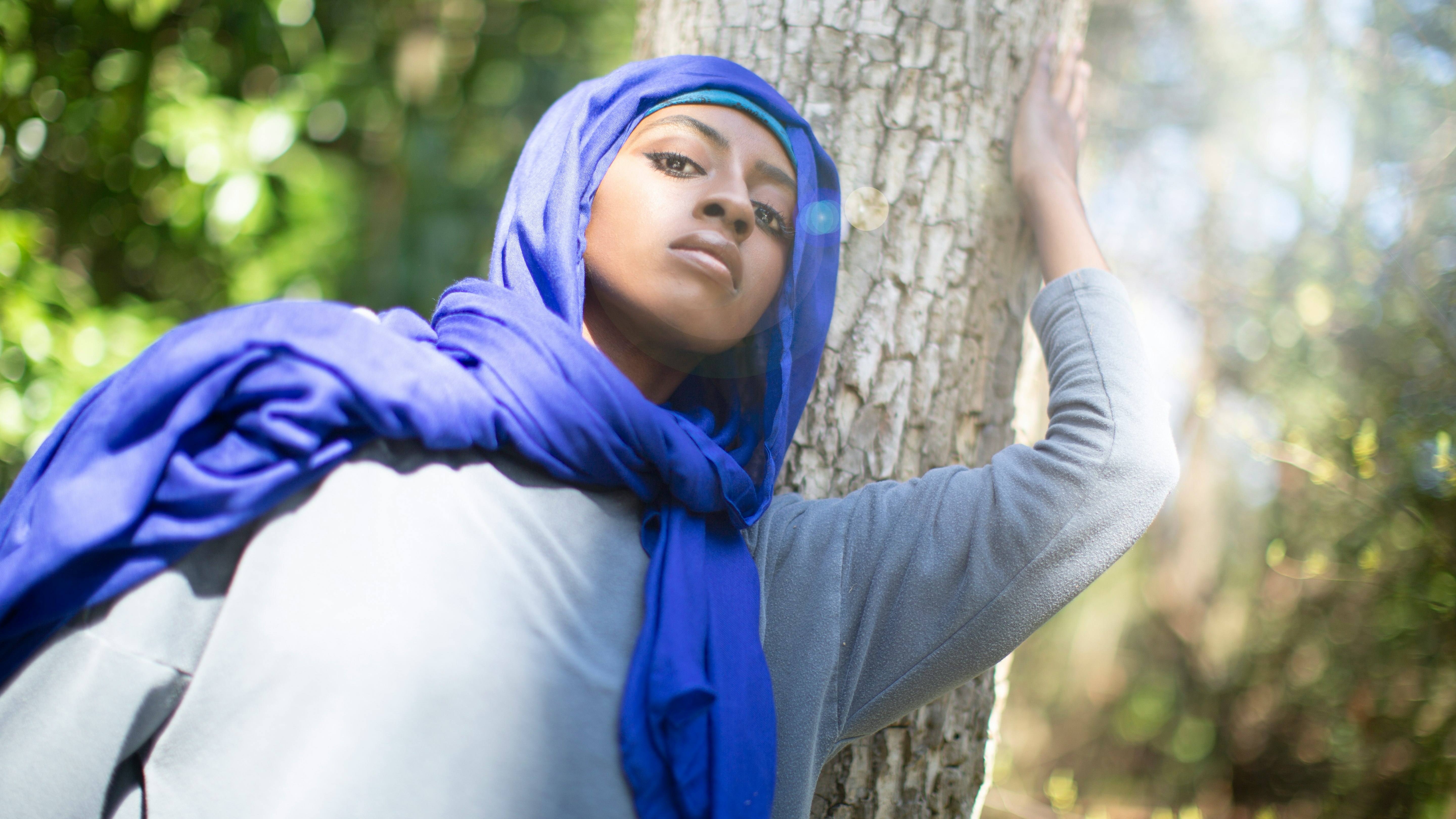 woman in blue hijab leaning on brown tree trunk